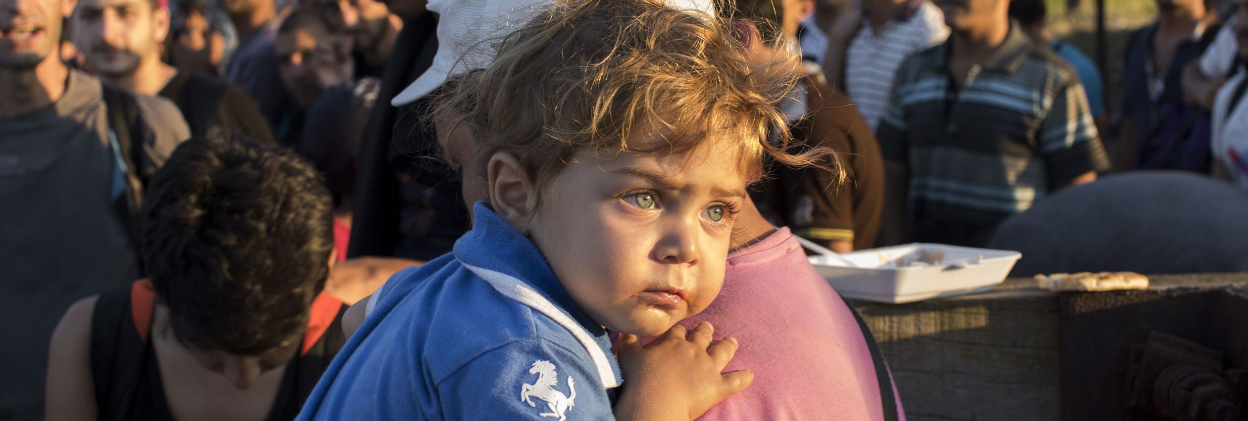 A Syrian refugee holds his son as they wait to move closer to crossing the border between Greece and the Former Yugoslav Republic of Macedonia.