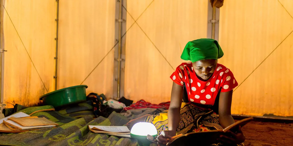 A refugee woman in Tanzania studies by lamplight.