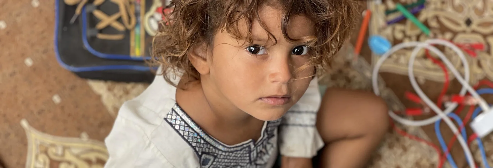 Girl with notepad looks at camera. Displaced Yemeni girl, Umaimah, practices writing in her makeshift shelter.