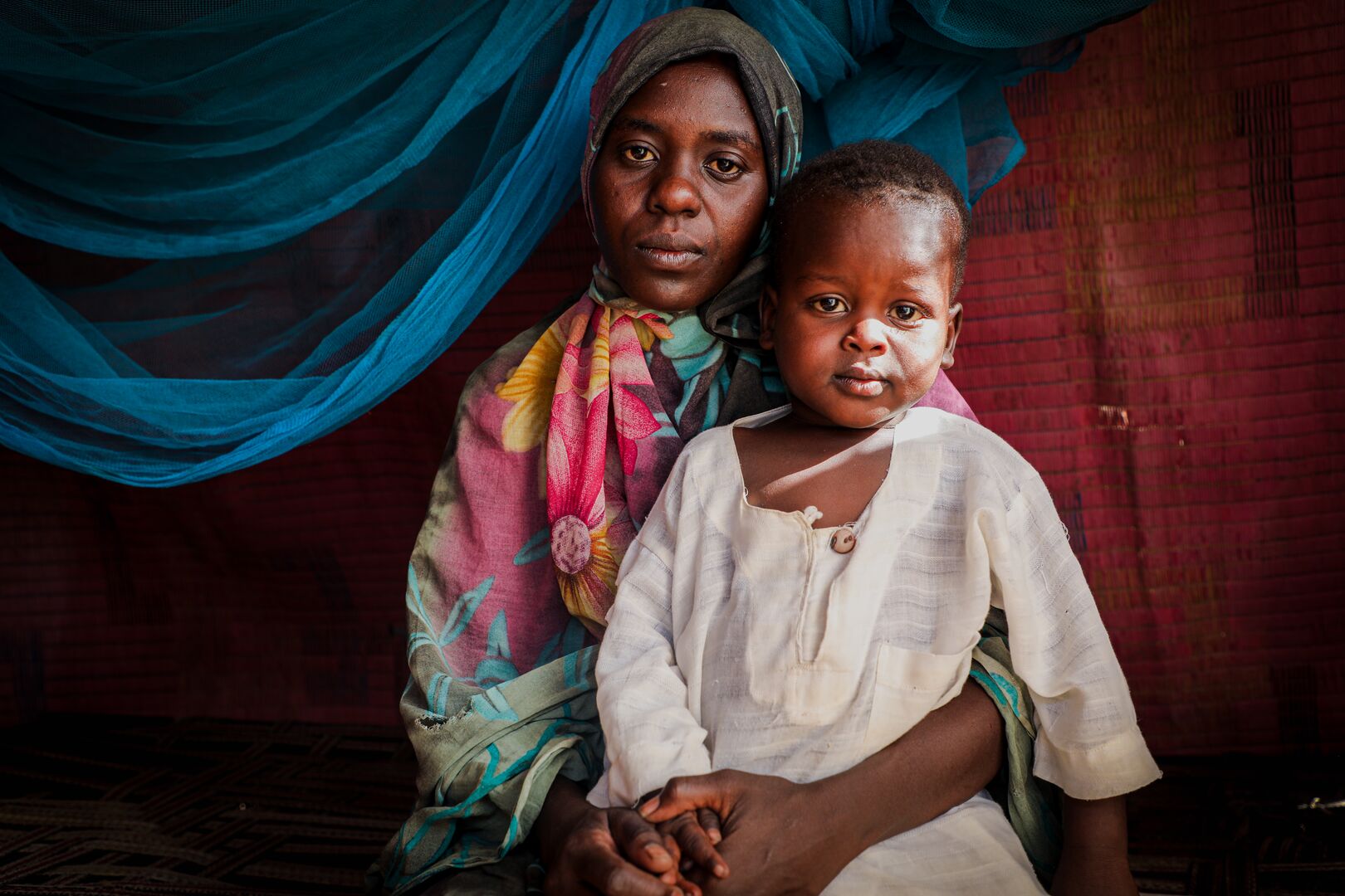 A Sudanese mother and child sit together, looking at the camera. 