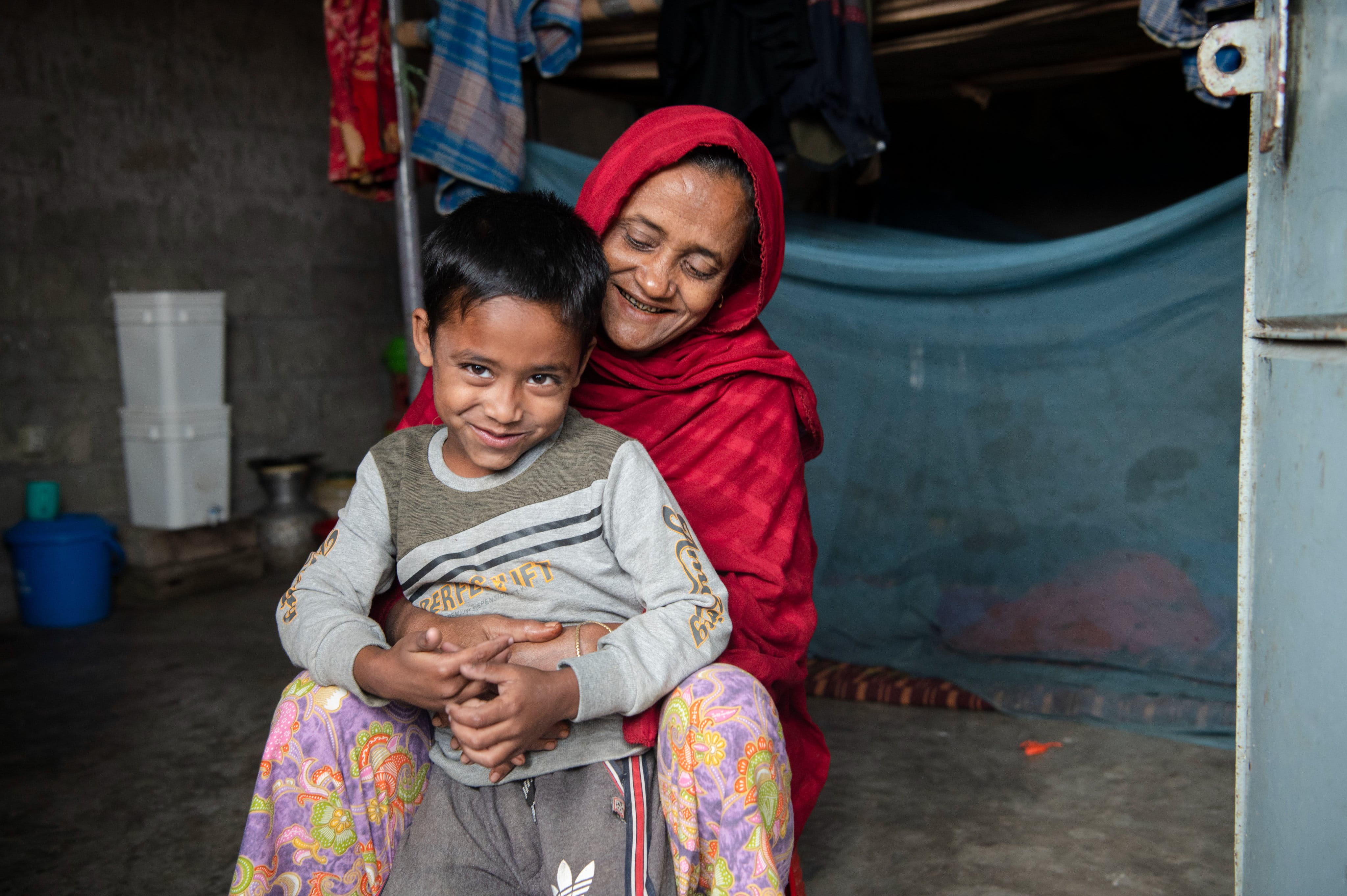 A Rohingya woman and boy sit together outside their shelter