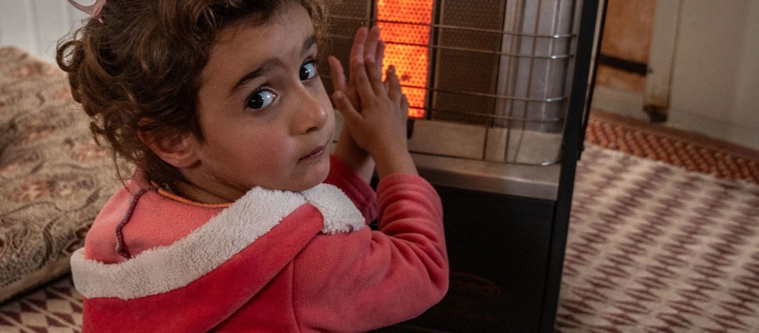 Emarat, a five-year-old Syrian girl, warms herself in front of her family's gas heater in their shelter in Za'atari refugee camp, Jordan.