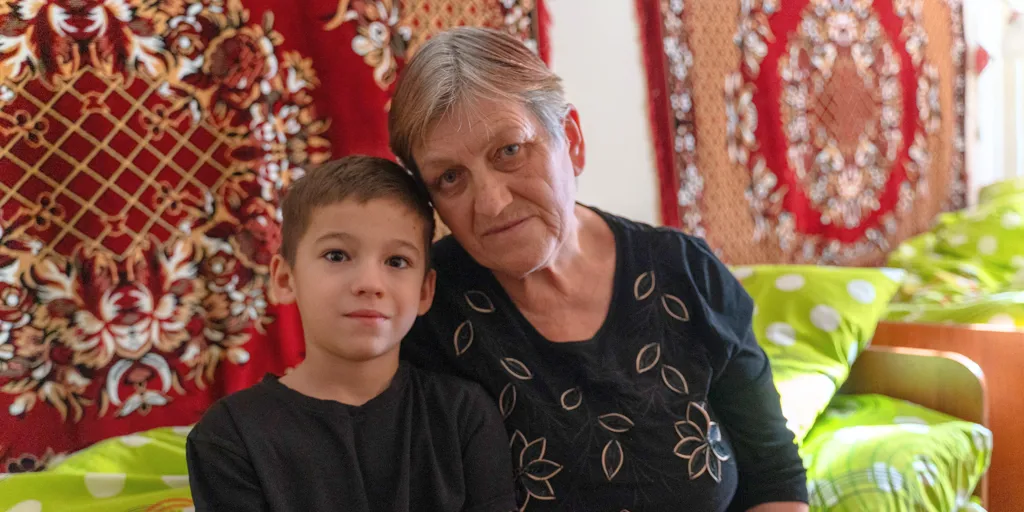 Kateryna and her grandson smile as they sit on a bed at a centre for displaced families in Zaporizhzhia, Ukraine.