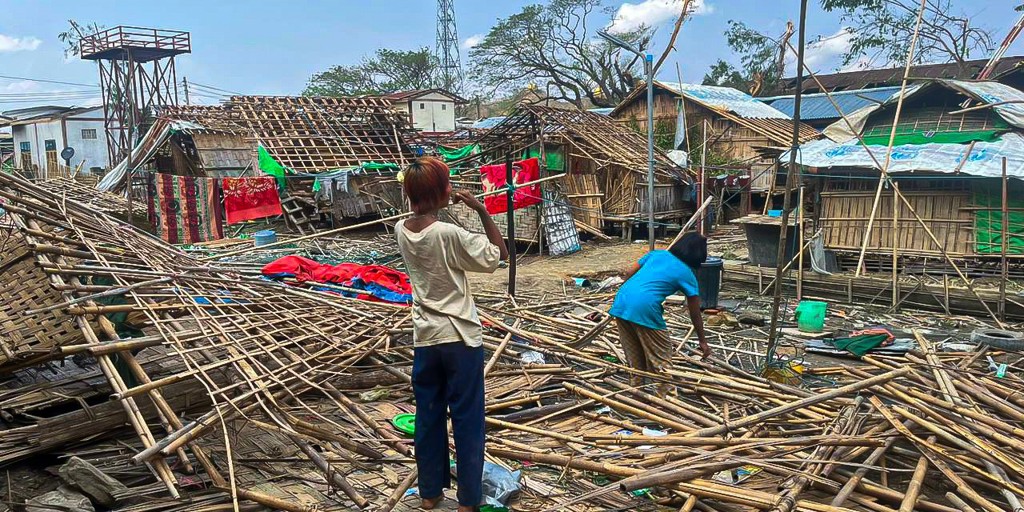 Two refugees in the middle of destroyed shelters in Rakhine state. Shelters at Kyauktaw City Hall IDP site in Rakhine State (Central) which have been destroyed during cyclone Mocha ; Humanitarian needs in Rakhine State and North West Myanmar were already dire before the cyclone hit, with approximately six million people already in need of relief aid