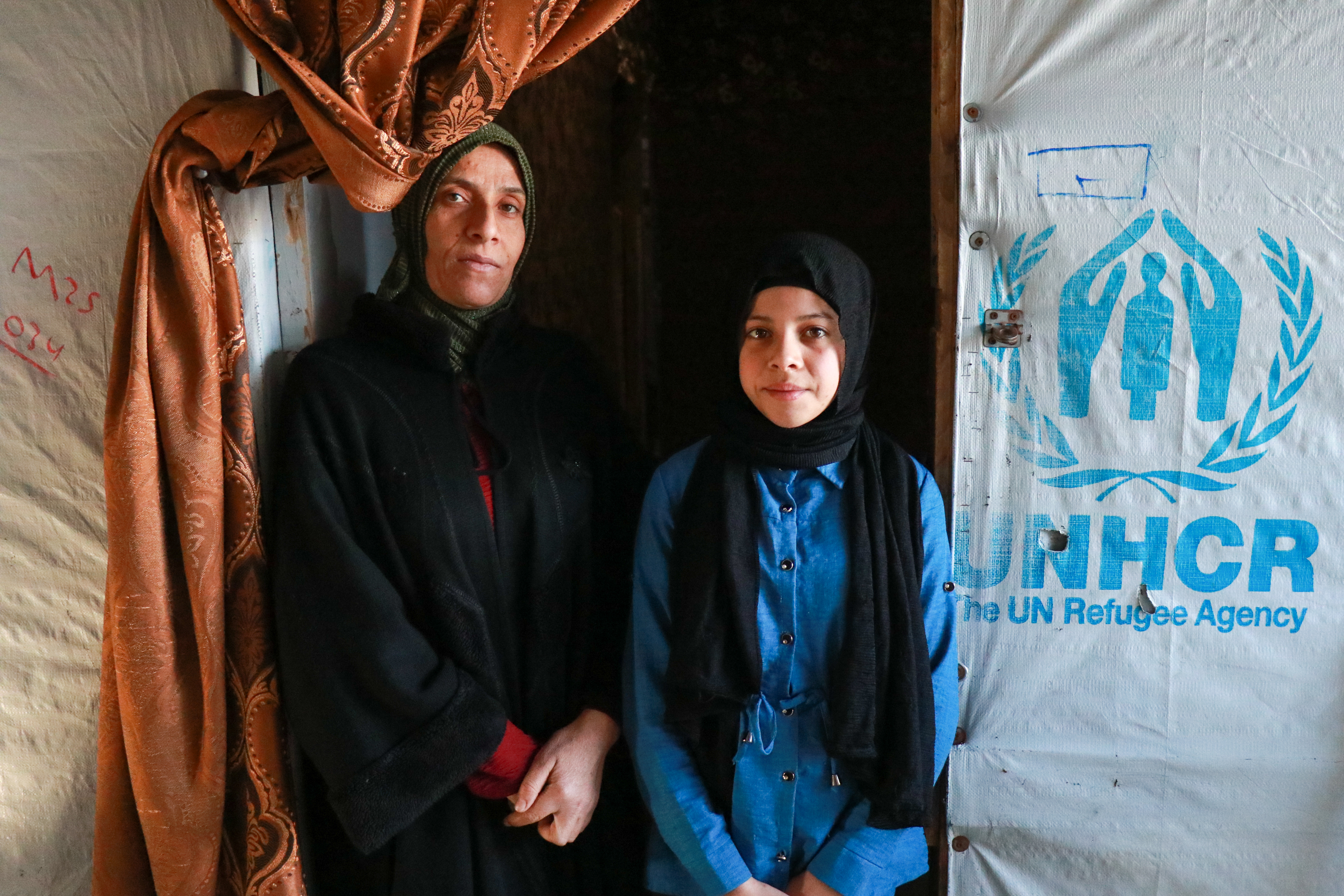 A mother and daughter stand in the doorway of their UNHCR tent in Lebanon