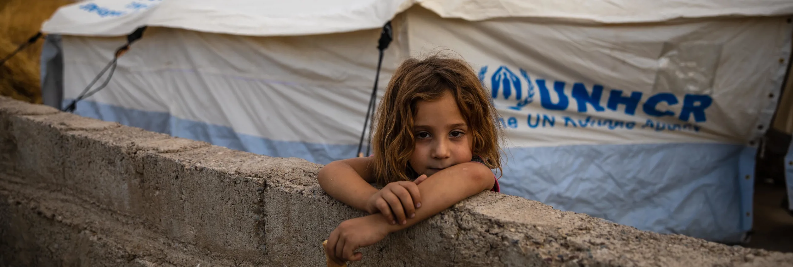 Eight-year-old Raghda Abbas Suleiman looks over a wall near her shelter at Bardarash camp in Duhok, Iraq, a day after arriving with her family.