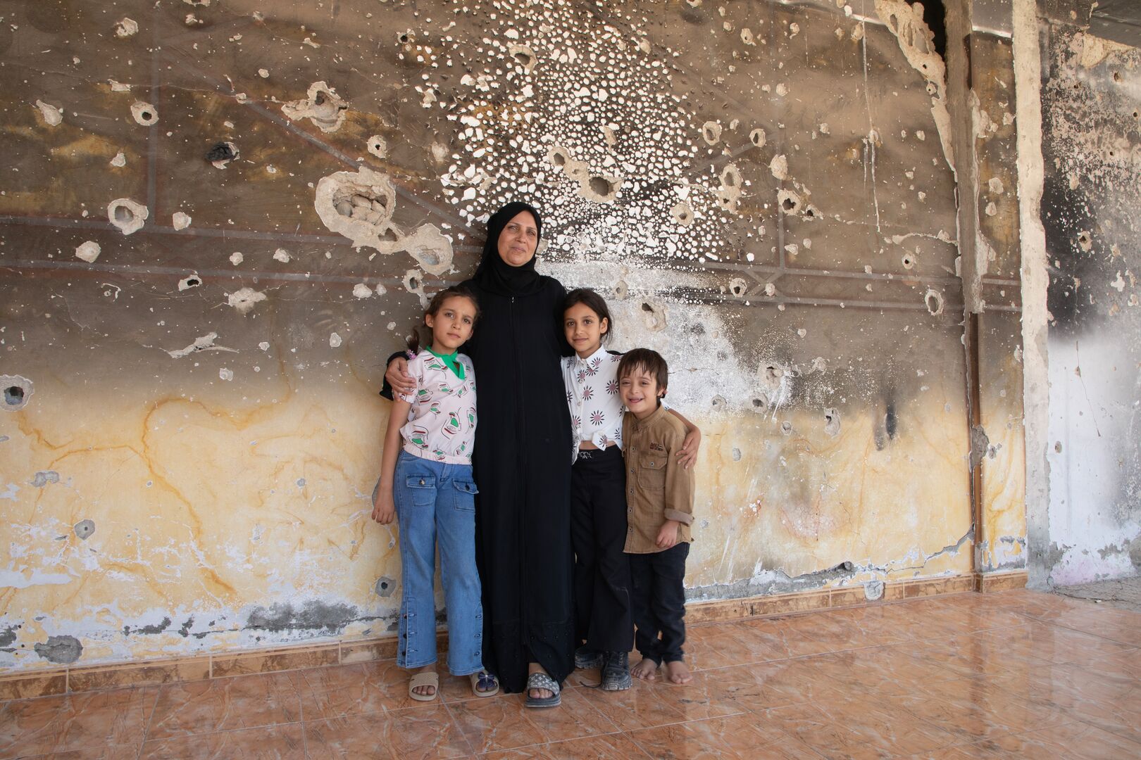 Basmah, 54, stands with her granddaughter Islam in the living room of their damaged home in Al Mansheya, Dar’a Governorate, after returning home.