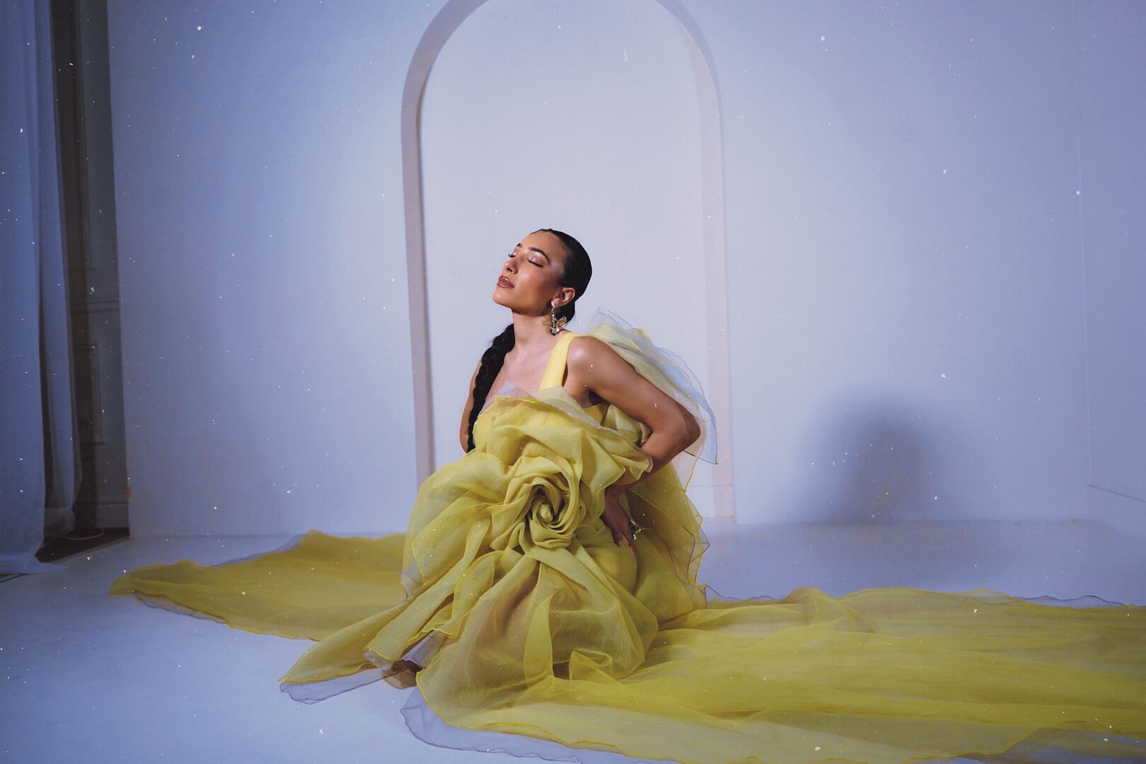 NOURI sits on a stage floor wearing a voluminous yellow dress