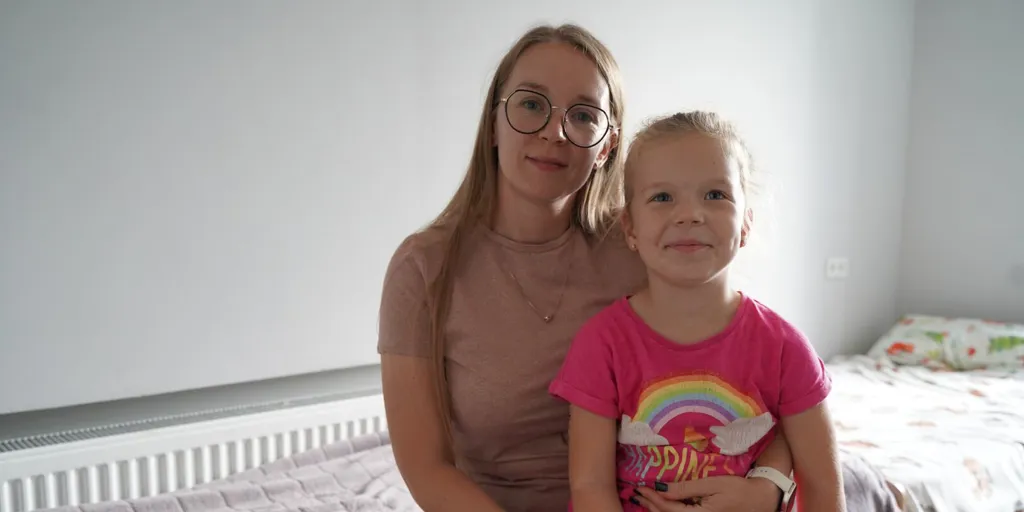 Displaced Ukrainians Nadiia and her daughter, Valentyna, smile while sitting at the foot of a bed in their home at a centre for displaced families in the Poltava region.