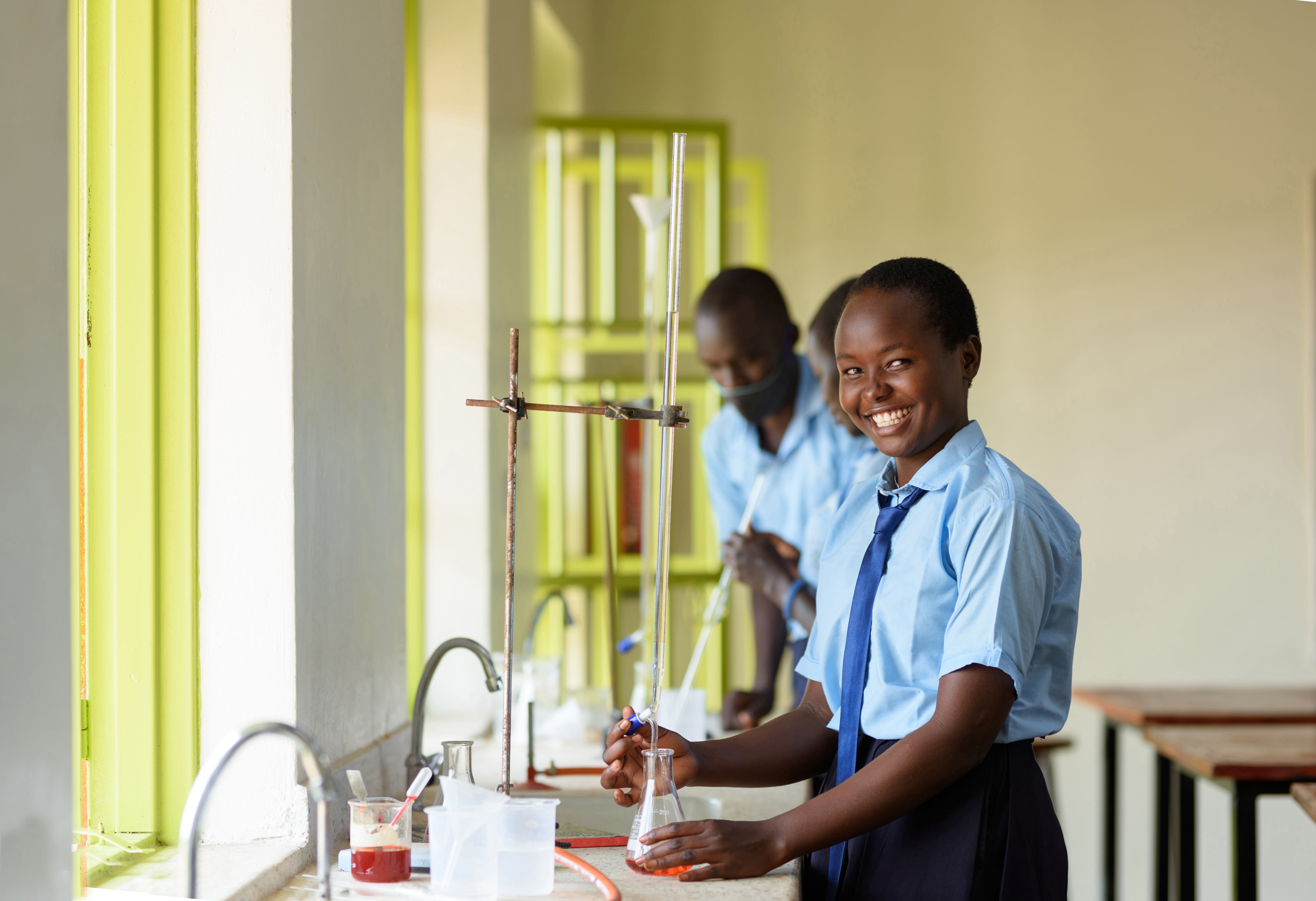 Young girl in school uniform smiles at camera. South Sudanese refugee, Sophie during a chemistry class in Uganda. 
