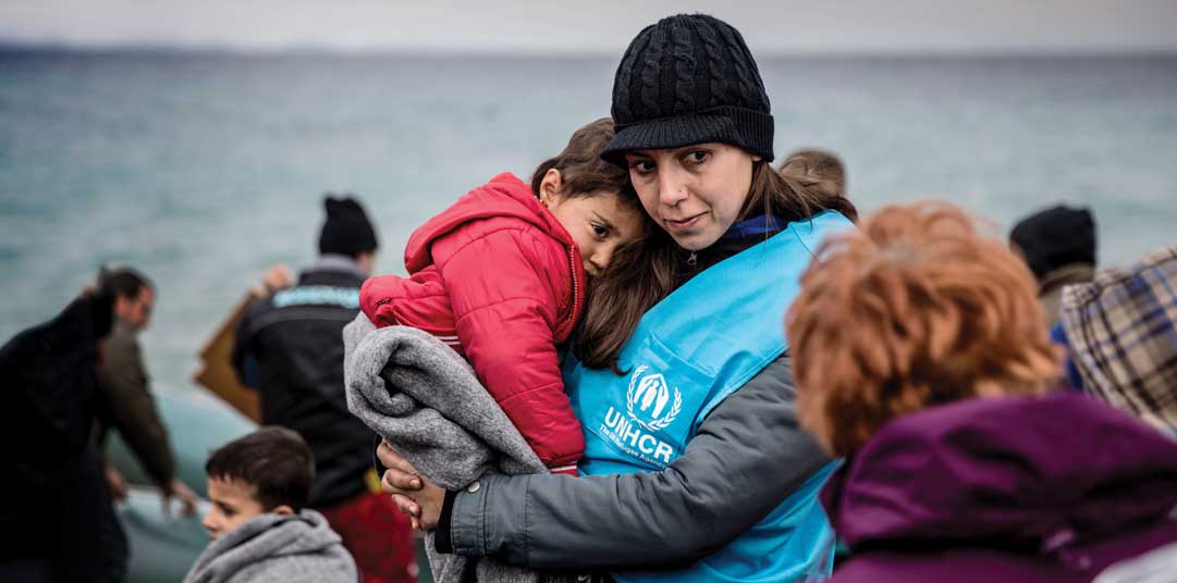A UNHCR staff member holds a young refugee boy in a blanket, after his boat landed on the Greek island of Lesvos.